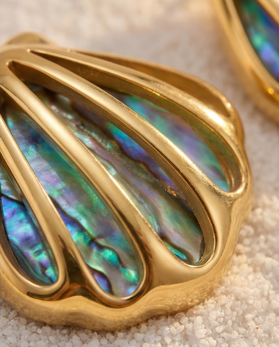 Gold shell-shaped earrings with colorful interior on a textured surface