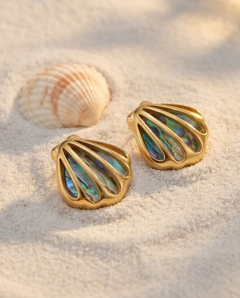 Gold shell-shaped earrings with colorful interior on a sandy surface