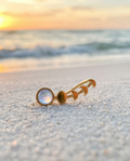 Gold ear climber with moonstone on a sandy beach at sunset