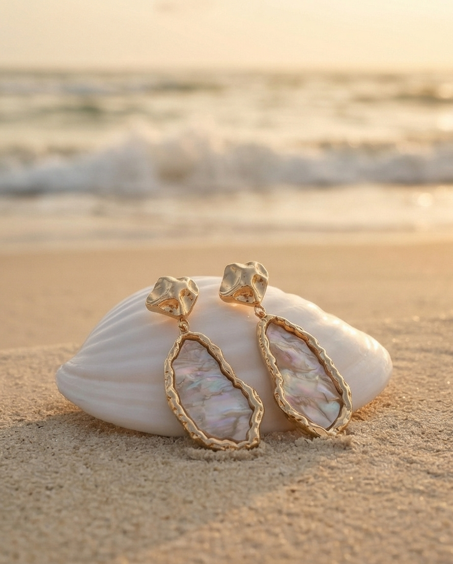 Gold earrings on a seashell with a beach background